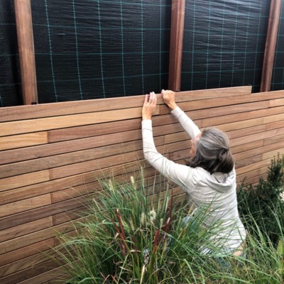 A woman easily installing a modern slatted fence using 7.0 cm wide Ipé hardwood slats, featuring our 5mm spacer clips and click-system.